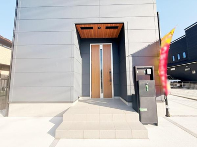 シンプルでスタイリッシュな玄関デザインです。直線的なフォルムが現代的な印象を与えます。玄関前のポストや宅配ボックスも便利に設置されています。明るい色合いのドアがアクセントになっています。