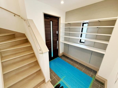 玄関スペースが広く収納棚が充実しています。シンプルで清潔感のある内装が特徴です。窓からの自然光が玄関を明るくしています。段差が低めの階段も使いやすい設計です。