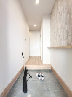 明るい照明が印象的な玄関です。広々とした空間で清潔感のあるタイル床が特徴です。壁面のデザインもアクセントになっています。段差があり使い分けしやすい設計です。収納や荷物の仮置きにも便利です。