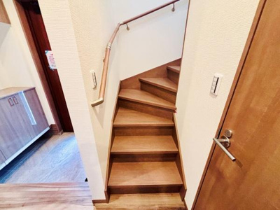 木目調の階段が落ち着いた雰囲気を演出しています。手すりが設置されており上り下りが安心です。周囲の壁面やドアとも調和したデザインです。コンパクトながらも空間を有効に使える設計です。