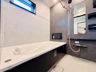 シンプルで洗練されたデザインのバスルームです。大きな鏡と窓が開放感を演出しています。機能的なシャワースペースとバスタブが配されています。壁面には収納棚が備わっています。床もお手入れがしやすい仕様です。