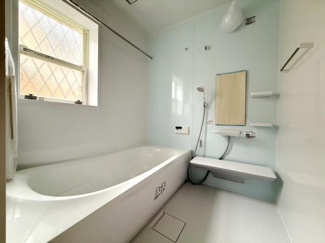 窓から自然光が入るバスルームです。浴槽と洗い場が広く設計されています。壁面は明るい色で清潔感が感じられます。便利な棚やミラーも設置されています。防水性のある床材もポイントです。