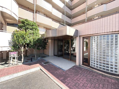 エントランスはガラス張りで開放感があります。植栽が整えられた外観が印象的です。広々としたアプローチが設計されています。建物全体が手入れされている様子がわかります。角ばったデザインが特徴的です。