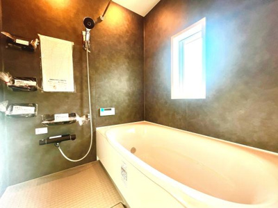 落ち着いた色合いの壁面が印象的なバスルームです。窓からの光がほどよく差し込み明るさを感じられます。浴槽はゆったりとしたサイズ感でシャワー設備もしっかりしています。収納スペースも豊富に備わっています。