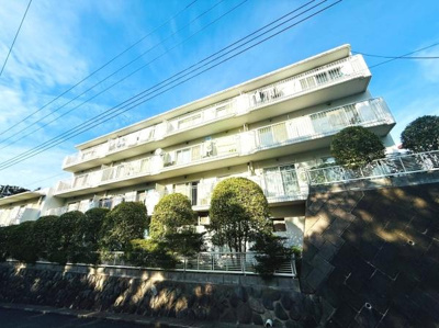 外観は明るい印象でバルコニーが広々としています。建物前にはきれいに整えられた植栽が並んでいます。白を基調としたデザインが特徴です。高台に立地し開放感を感じられます。日当たりの良さも魅力の一つです。