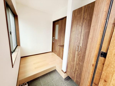 玄関には大きな収納スペースが設けられていて整理整頓しやすい仕様です。木目調のデザインが温かみを感じさせます。シューズボックスがあり靴の収納にも便利です。窓があるため明るい採光も確保されています。