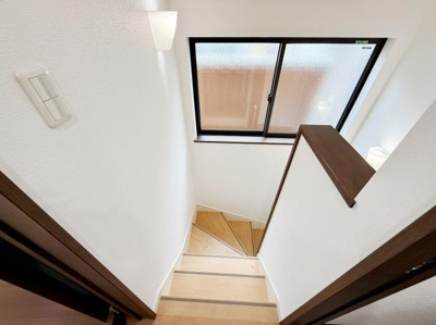 階段に設けられた窓から自然光が差し込み明るい空間を演出しています。壁や手すりの落ち着いた色合いが調和しています。階段部分はスペースを有効に活用したコンパクトな設計です。