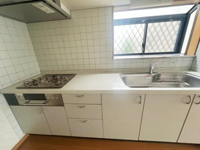 シンプルで使いやすいキッチンです。広めのシンクで作業がしやすい仕様となっています。ガスコンロと収納がバランス良く配置されています。窓があり採光も確保されています。