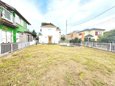 開放感のある現地土地写真です。周囲には住宅が並び静かな環境がうかがえます。整地された敷地で利用しやすい形状が特徴です。柵で囲まれており安心感があります。日当たりも期待できる立地です。