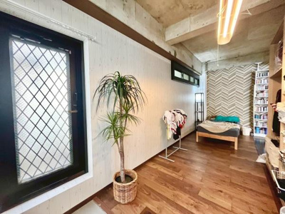 木目調のフローリングと白い壁が調和した寝室です。天井のコンクリートとスタイリッシュな照明が個性的な空間を演出します。窓からは自然光がしっかり入り開放感もあります。