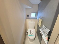 コンパクトな空間で使い勝手に配慮されたトイレです。小窓から光が入り明るい雰囲気が広がります。壁面の一部にアクセントカラーが施されています。手洗いやペーパーホルダーも設置されています。