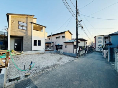 幅のある前面道路が見える現地写真です。周囲には住宅が並び落ち着いた雰囲気が広がっています。新築物件の外観も確認できます。車の出し入れもしやすい環境です。静かな住宅街の一角に位置しています。