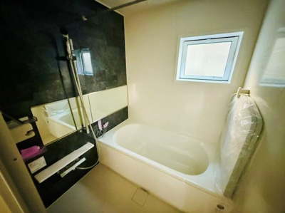 壁面のダークカラーと明るい浴槽のコントラストが印象的です。窓付きで採光や換気もしやすいバスルームです。鏡が空間を広く感じさせます。バスタブの形状もゆったりしています。