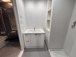 すっきりとしたデザインの洗面台が設置されています。収納スペースも備え付けられており日用品の整理に便利です。清潔感のある空間が広がっています。隣接する棚も使い勝手が良いです。