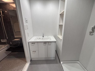 すっきりとしたデザインの洗面台が設置されています。収納スペースも備え付けられており日用品の整理に便利です。清潔感のある空間が広がっています。隣接する棚も使い勝手が良いです。