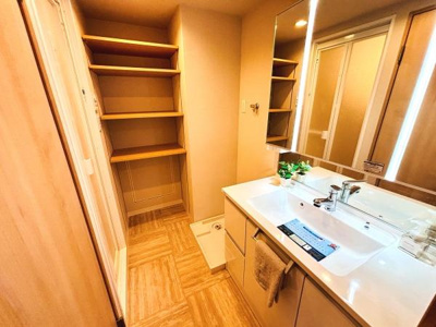 洗面台は明るい照明が設置されており使いやすい空間です。収納棚も複数あり整理整頓がしやすいです。洗濯機置き場も備え付けられているので便利です。清潔感のある色合いが室内全体に広がっています。