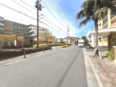 ゆったりとした道路幅があり車の出入りもスムーズに感じられます。周囲の建物は統一感のあるデザインで明るい色合いが印象的です。植栽や街路樹が整備されており開放感のある町並みです。