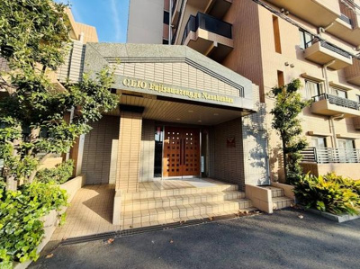 落ち着いた色合いの外観が印象的なエントランスです。清潔感のあるタイルと植栽が調和しています。段差もスムーズに上がれる設計となっています。建物名が分かりやすく表示されています。周辺の緑も魅力の一つです。