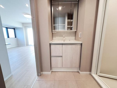 落ち着いたトーンの洗面台は空間全体に統一感をもたらします。鏡収納も付いており使い勝手が考えられています。清潔感のある床材と隣室への導線もスムーズです。収納力も確保されていて日常使いに便利です。