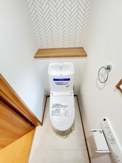 淡いトーンの床と壁が清潔感を演出しています。トイレ背面のヘリンボーン柄がさりげないアクセントになっています。手すりやペーパーホルダーが設置され使いやすさにも配慮されています。