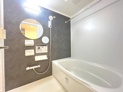 明るい照明が特徴の浴室です。壁面には便利な鏡と収納棚が設置されています。モダンなデザインのバスタブが印象的です。グレーの壁面が空間を引き締めています。換気もしやすい設備が揃っています。