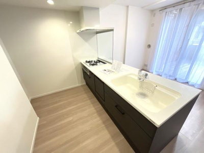 明るい空間に溶け込むシンプルなキッチンです。収納スペースが確保されており作業台も広々としています。窓から光が差し込み開放感が魅力のキッチンとなっています。ダークカラーの収納が空間を引き締めます。