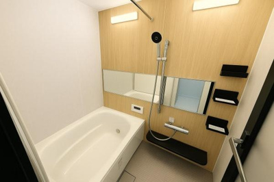 木目調のアクセントパネルが空間にやわらかな印象を与えます。横長のミラーが高級感を演出しています。壁面収納も備わっていて使い勝手に配慮されています。浴槽はゆったりとした形状です。