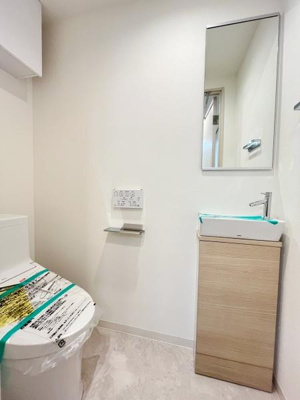 清潔感のあるシンプルなトイレ空間です。手洗いカウンター付きで使いやすいレイアウトになっています。壁付けのペーパーホルダーや操作パネルもスッキリと配置されています。全体が明るく開放的な印象です。