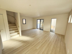 リビングは開放感を感じられる広々とした空間です。窓から自然光が差し込み室内が明るくなっています。フローリングの色合いが空間をやさしく演出しています。階段や扉もすっきりとしたデザインです。