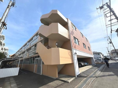 外観は明るい色合いで清潔感があります。建物の形が特徴的で遠くからも目を引きます。共用階段もゆったりとしており利用しやすい印象です。建物前には駐車スペースも確保されています。